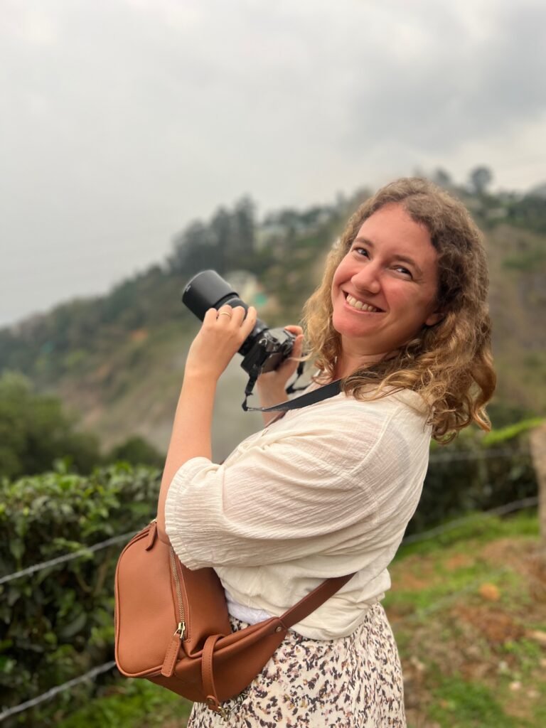 Jeune femme avec un appareil photo souriant à la caméra, montrant Auriane, fondatrice du service de Travel Planning Travel with Auri.